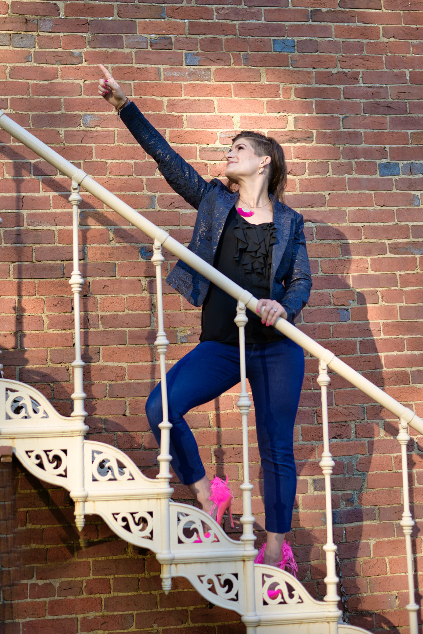 Dr. Andrea Moore wears bright pink high heels and jeans and lays in front of a gray brick wall in a photo promoting her Pain to Power Group for Chronic Pain.